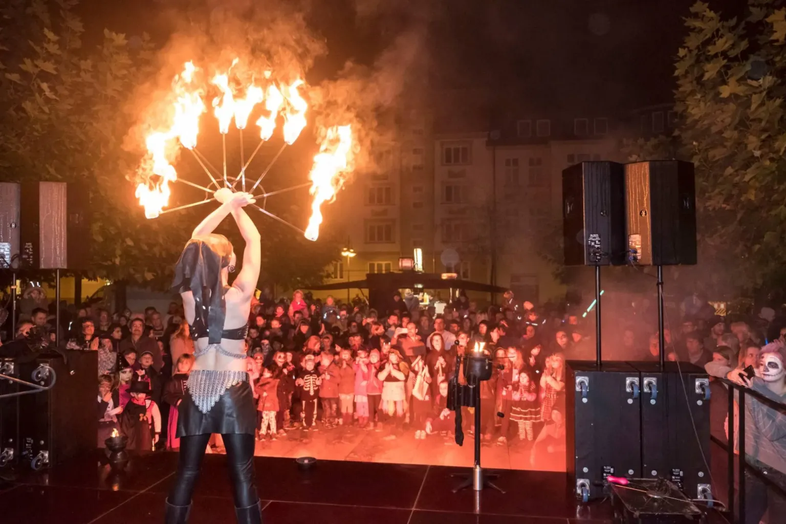 Feuerkünstlerin zeigt bei Dunkelheit einen brennenden Fächer vor dichtem Publikum
