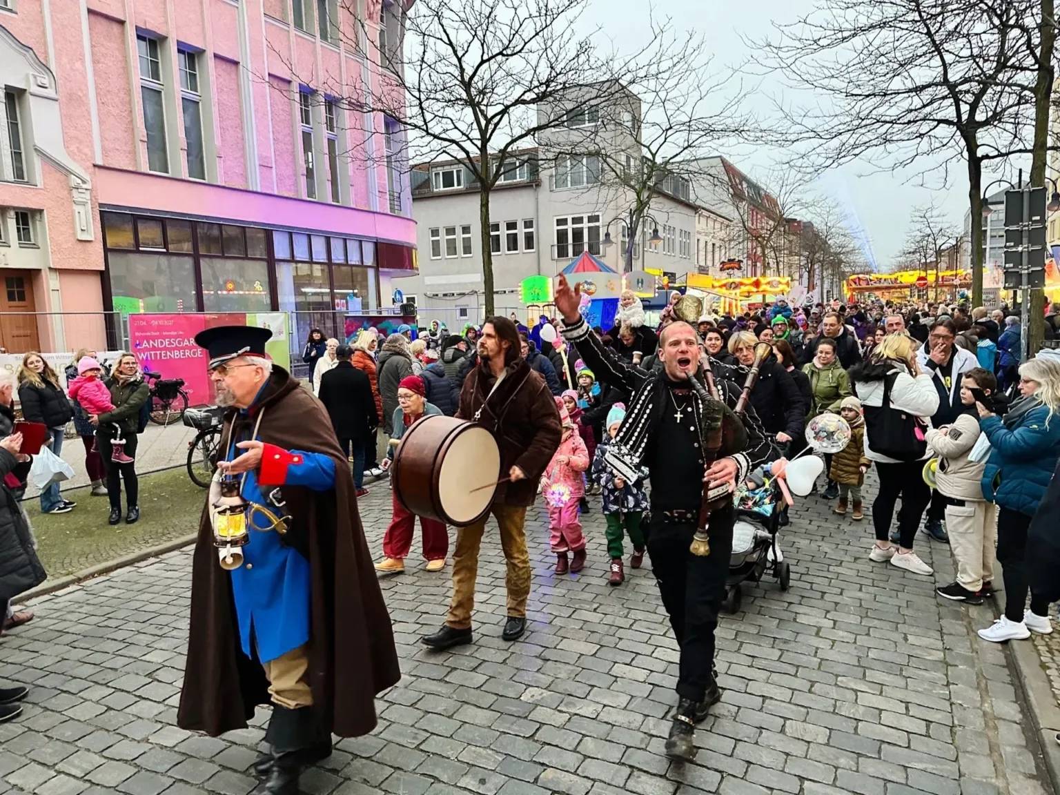 Laternenumzug mit Trommler und Dudelsackspieler in historischen Kostümen, dahinter Kinder mit Laternen
