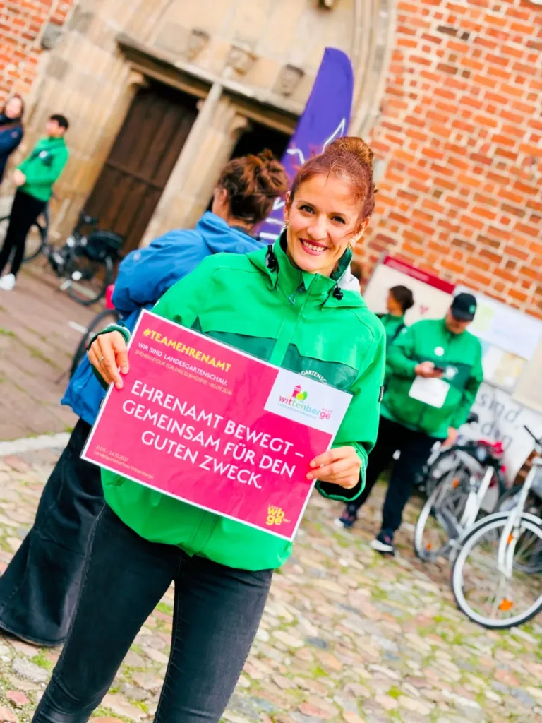 Eine Frau hält ein Schild, auf dem steht: Ehrenamt bewegt - gemeinsam für den guten Zweck